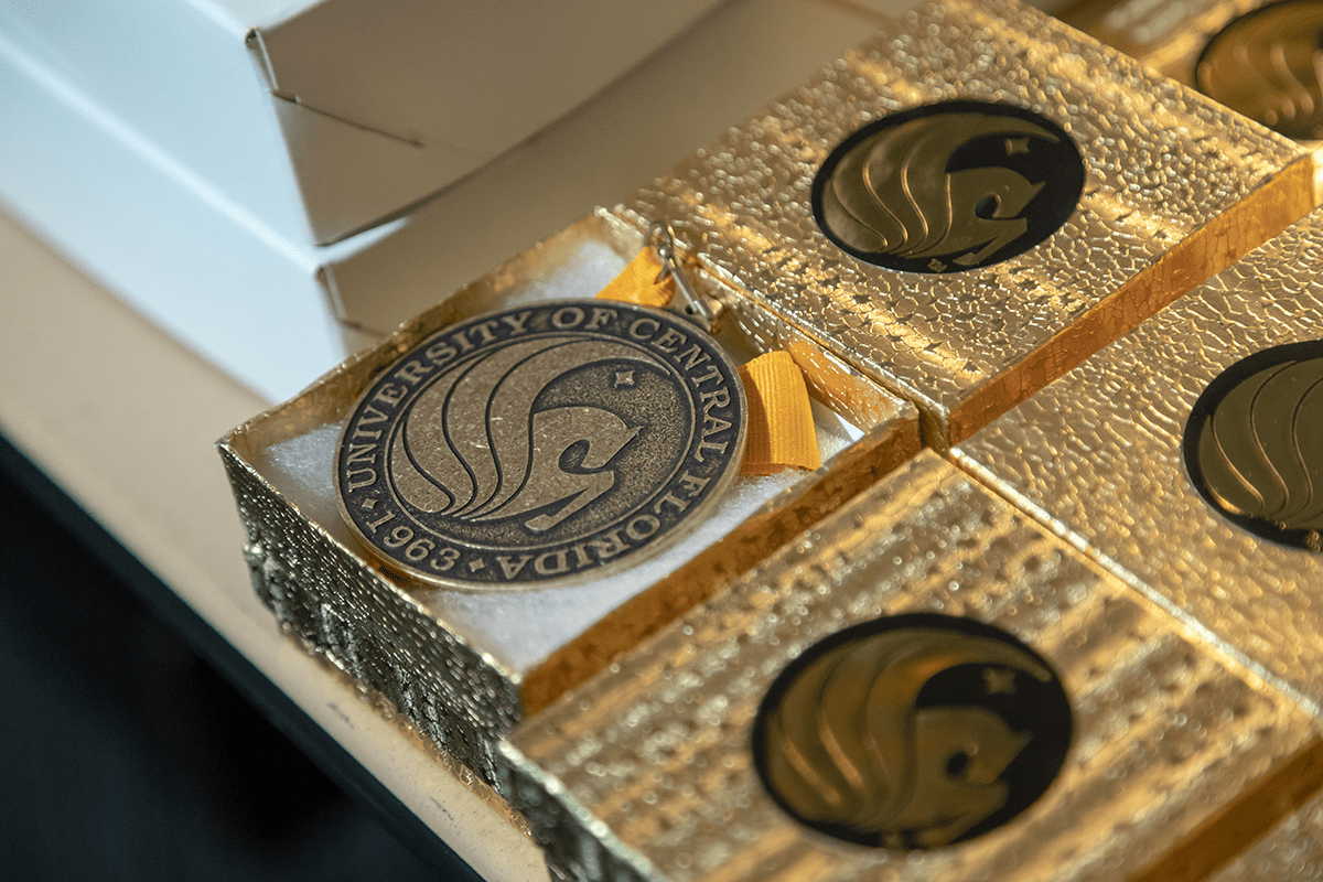 Gold and black medals featuring the University of Central Florida logo are displayed in gold boxes.